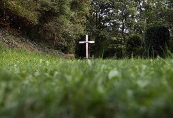 Langezogene Grasfläche. Im Hintergrund ist ein Kreuz aufgestellt.