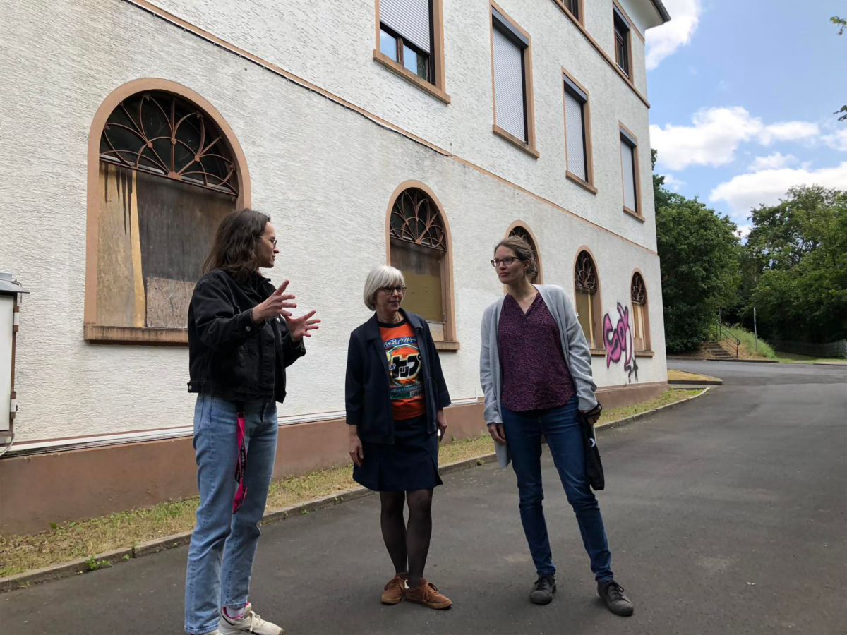 Drei Frauen stehen vor einem Gebäude. Sie sprechen miteinander und gestikulieren.